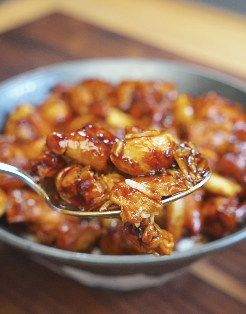 Spoon lifting glossy chicken and whole garlic cloves coated in a savory soy-based sauce from the Whole Garlic Chicken Stir Fry Recipe served over rice.