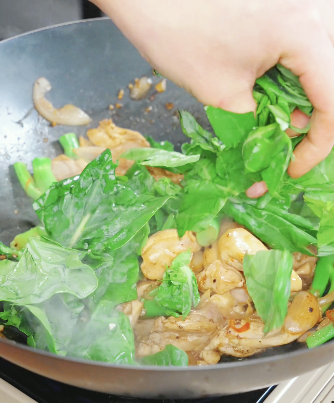 Fresh Chinese broccoli leaves being added to a wok while making a Drunken Noodles Recipe. The leaves wilt quickly and add color and freshness to the dish.