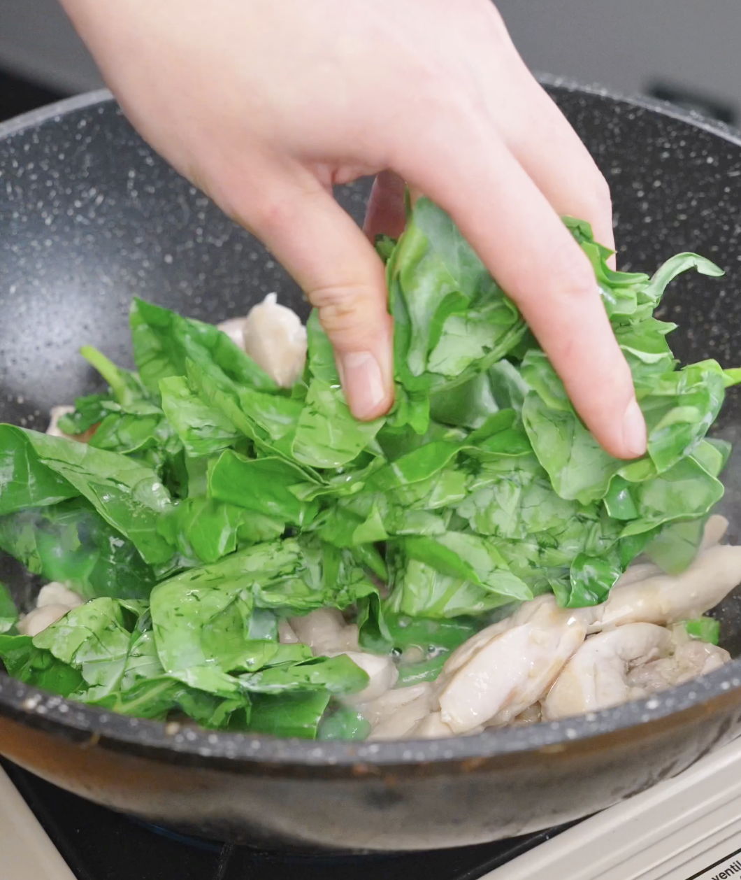 Fresh Chinese broccoli leaves being added to the pan to cook alongside the chicken and stems in this Pad See Ew Recipe.