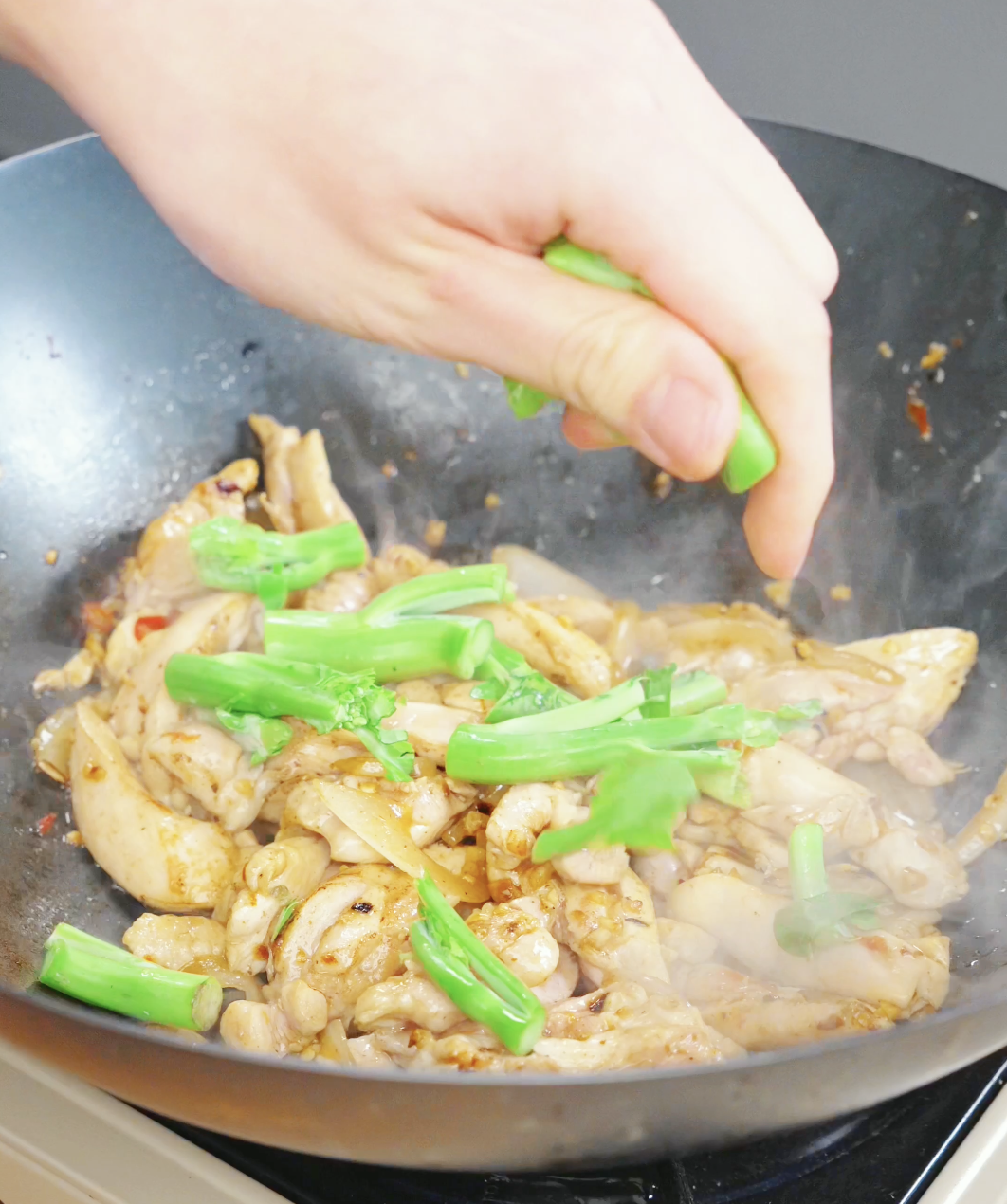 Chinese broccoli stems being added to a wok during a Drunken Noodles Recipe. The stems are cooked first to ensure they become tender while retaining texture.