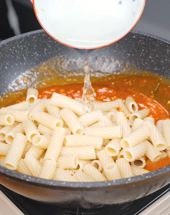Reserved pasta water being poured over the cooked rigatoni to create a silky, creamy sauce for this Gochujang Vodka Pasta Recipe.