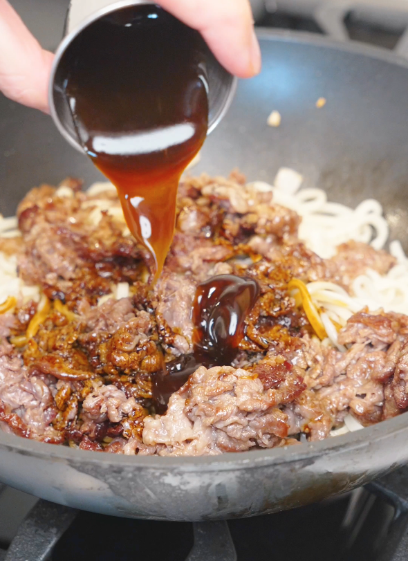 A savory soy and oyster sauce mixture being poured over beef and noodles for the Mongolian Beef Noodles Recipe.