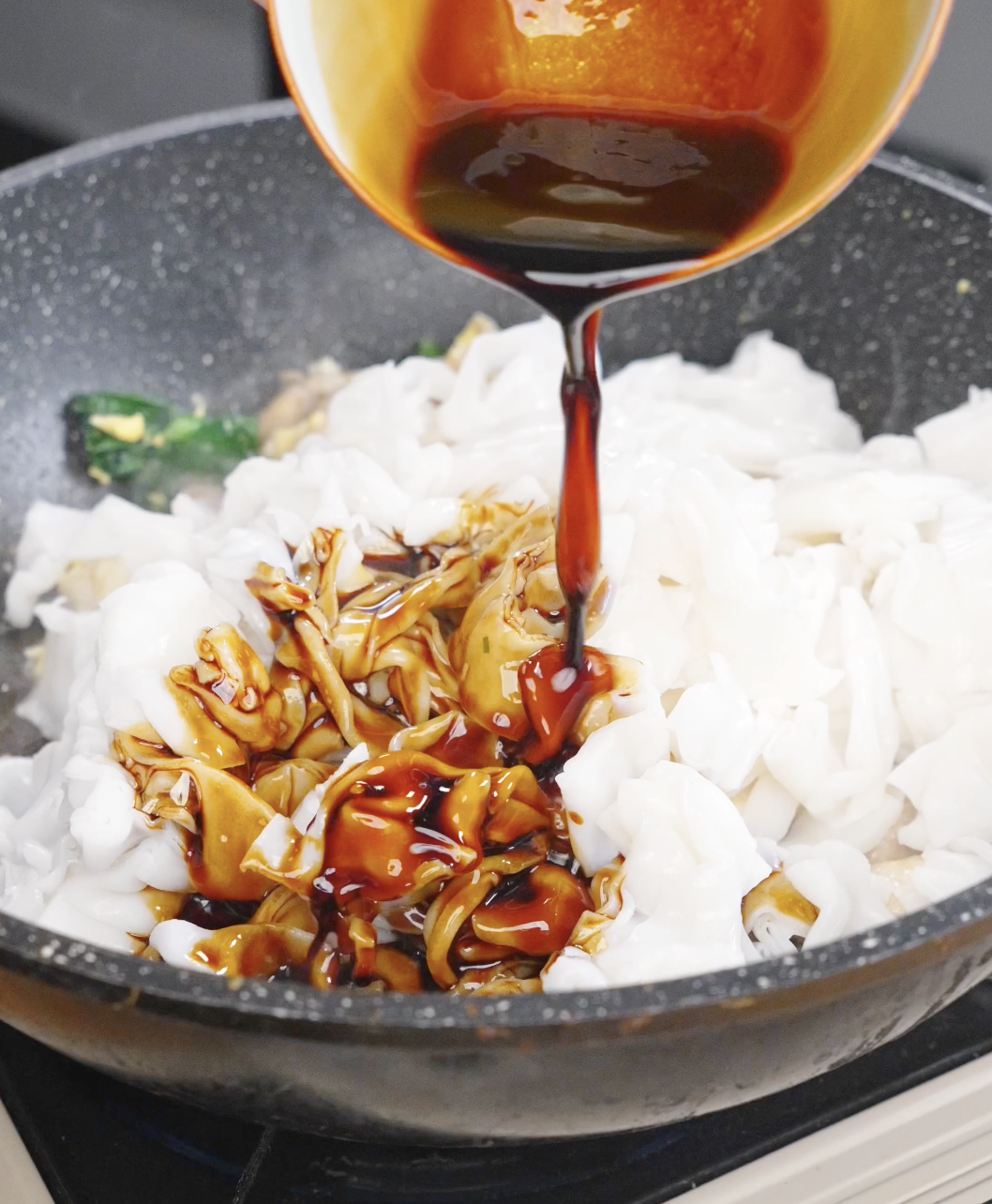 Prepared soy sauce mixture being poured over fresh wide rice noodles in the pan for this Pad See Ew Recipe.