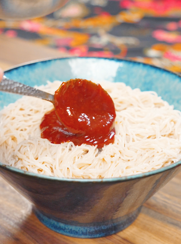 A spoonful of spicy gochujang sauce being poured over chilled noodles for this Spicy Cold Noodles Recipe.