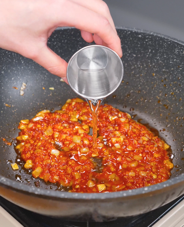 Vodka being poured into the pan to deglaze the cooked gochujang, onion, and garlic mixture for this Gochujang Vodka Pasta Recipe.
