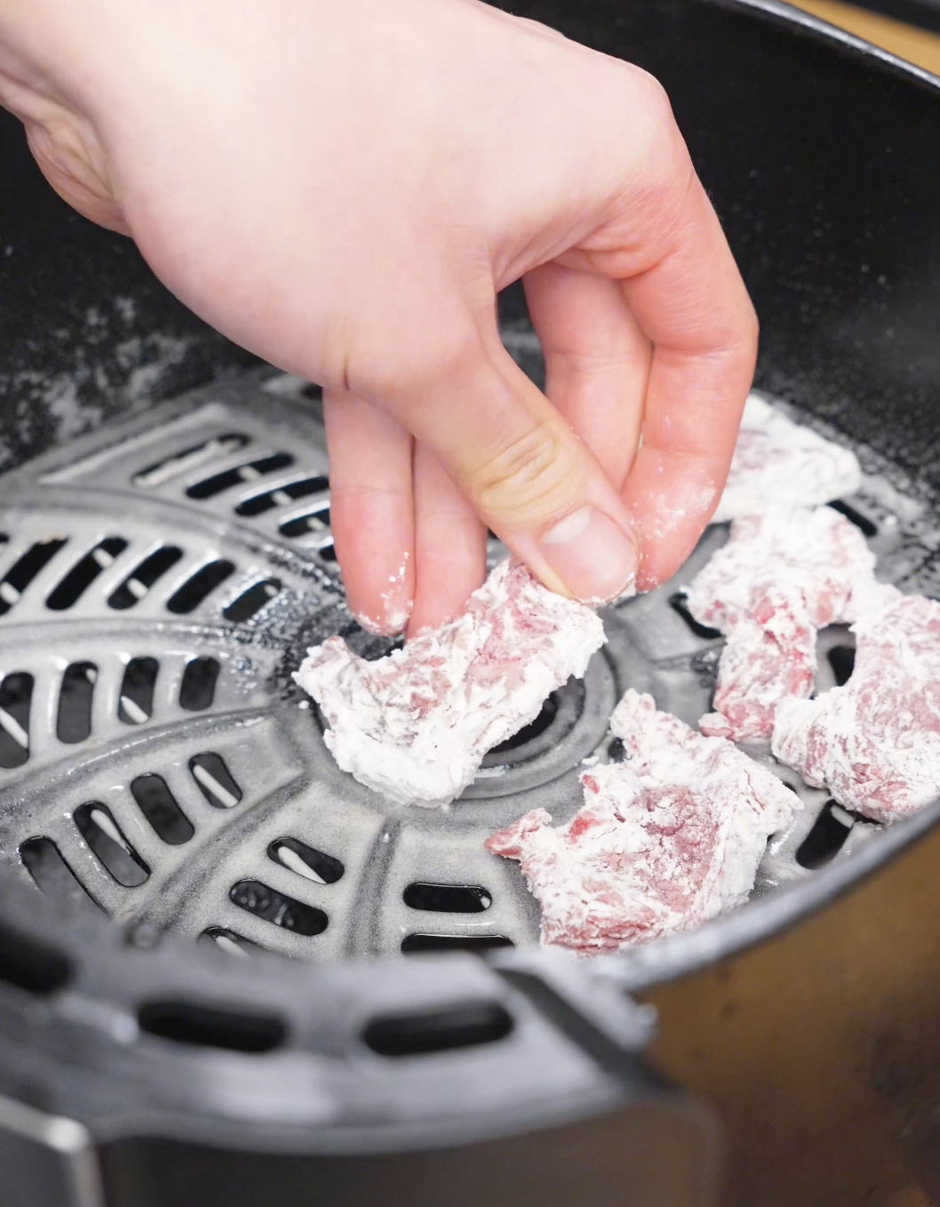 Coated pieces of flank steak being placed in an air fryer basket in a single layer before cooking for this Crispy Chili Beef Recipe.