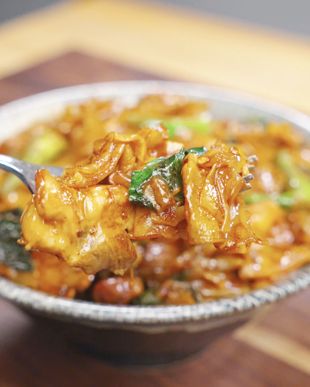 A fork lifting a bite of Pad See Ew Recipe with tender chicken, wide rice noodles, and Chinese broccoli coated in a savory sauce.