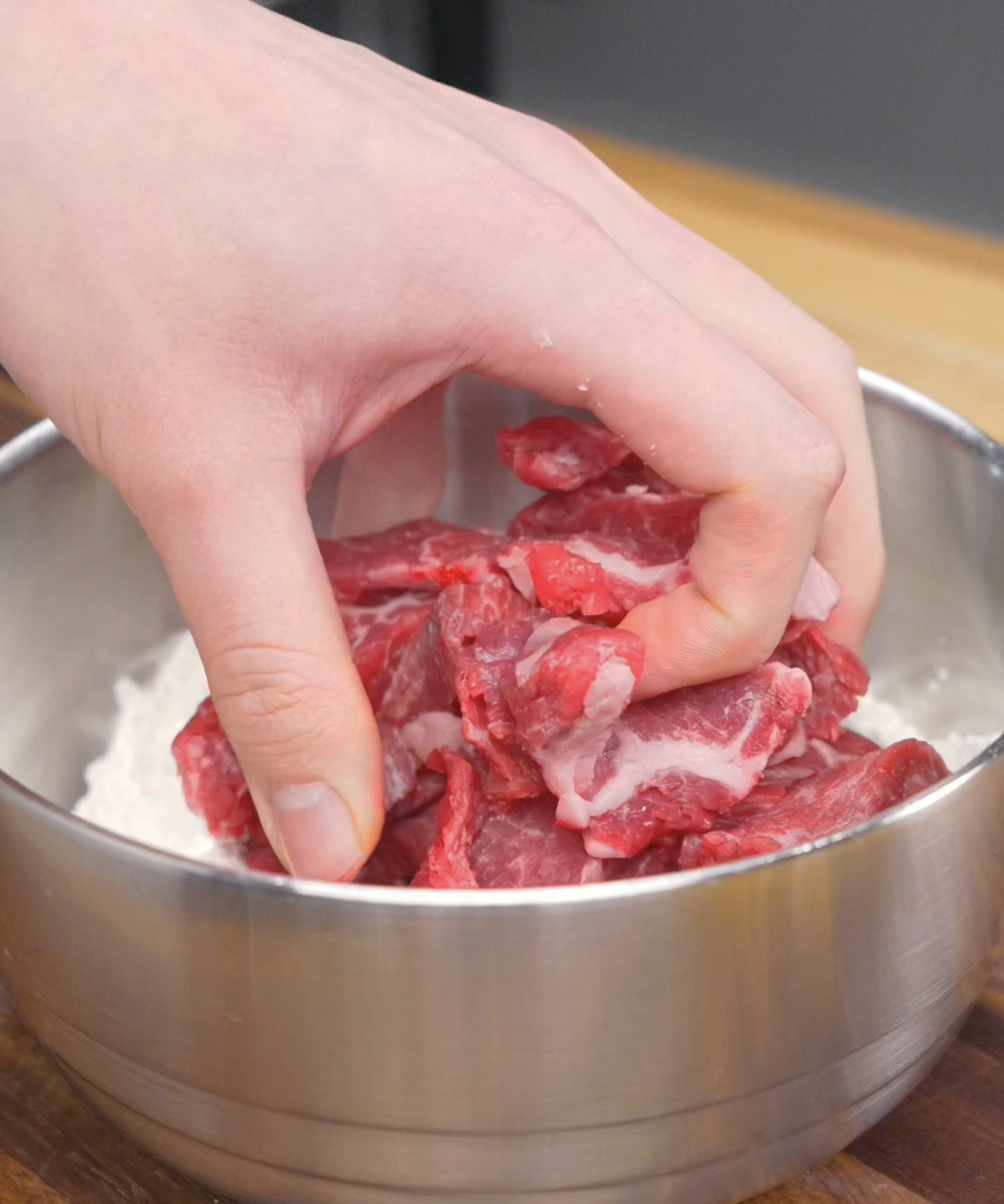 Thinly sliced flank steak being tossed in a flour and cornstarch mixture for a Crispy Honey Garlic Beef Recipe. Even coating ensures the beef becomes crispy and holds the sauce well.
