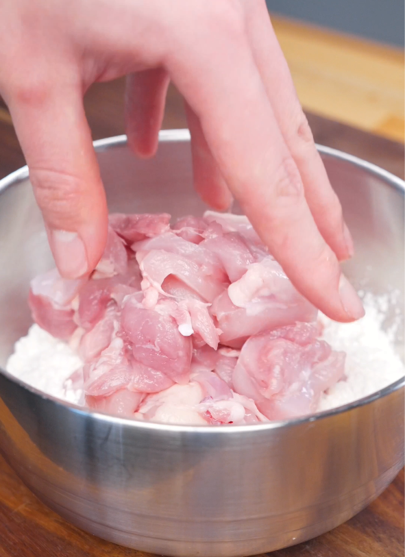 Chicken thigh pieces being dredged in a cornstarch and flour mixture before air frying for Crispy Chili Oil Chicken.