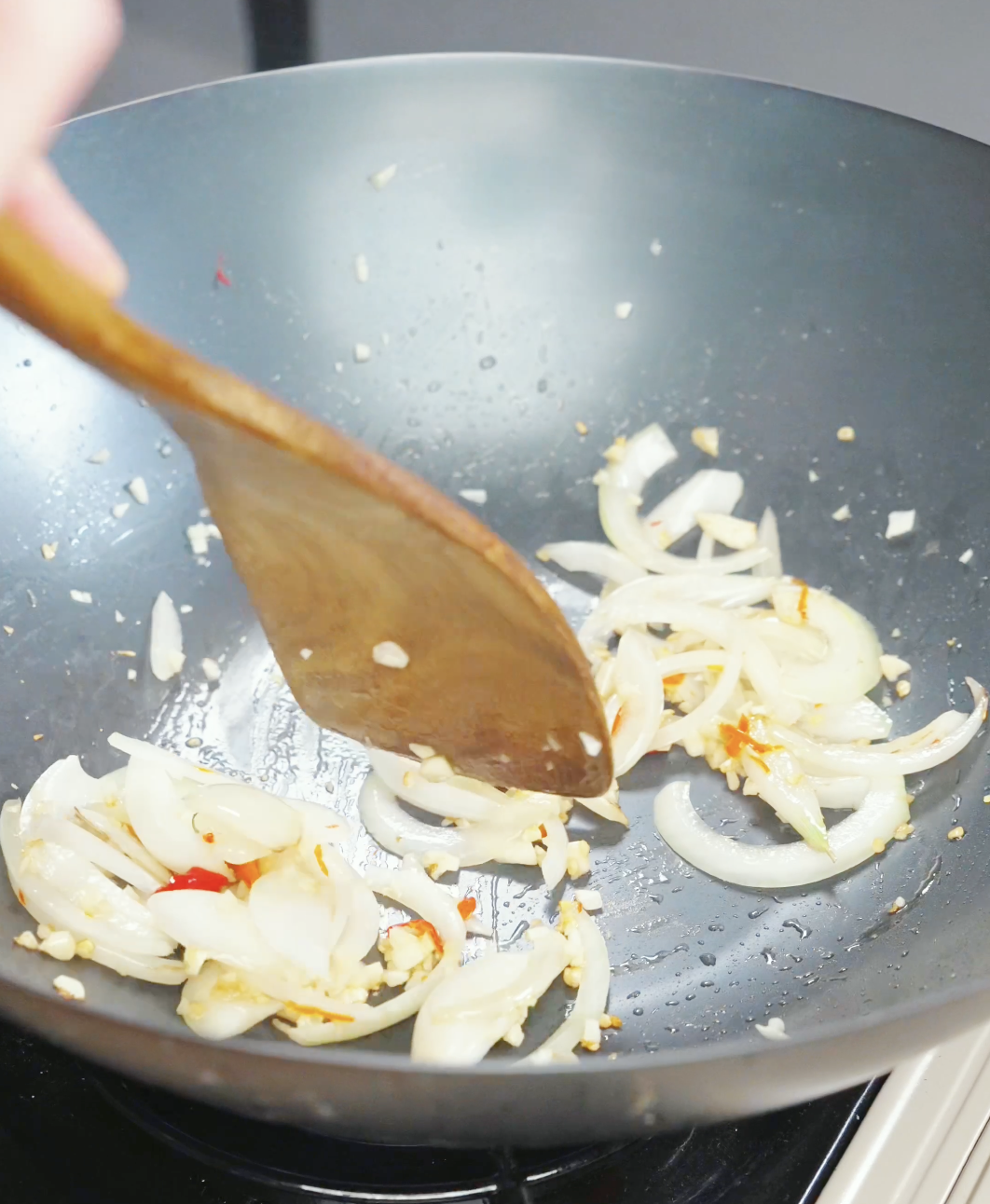 Onion, garlic, and Thai chilies sautéing in a wok while making a Drunken Noodles Recipe. The aromatics create the flavorful base of the stir fry.