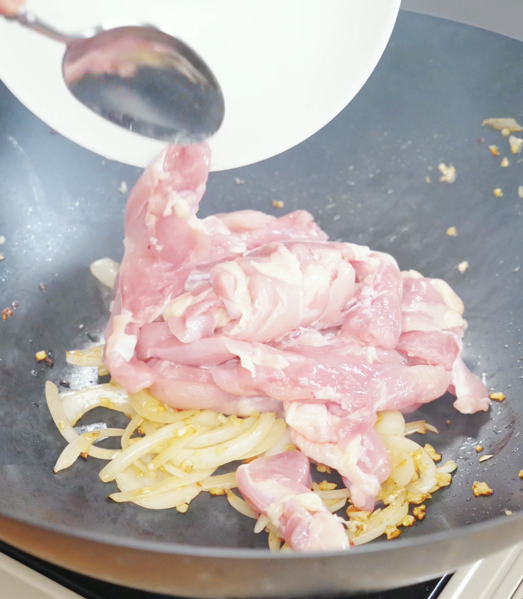 Thinly sliced chicken thighs being added to a wok with onions, garlic, and chilies for a Drunken Noodles Recipe. The chicken cooks quickly before the noodles and vegetables are added.