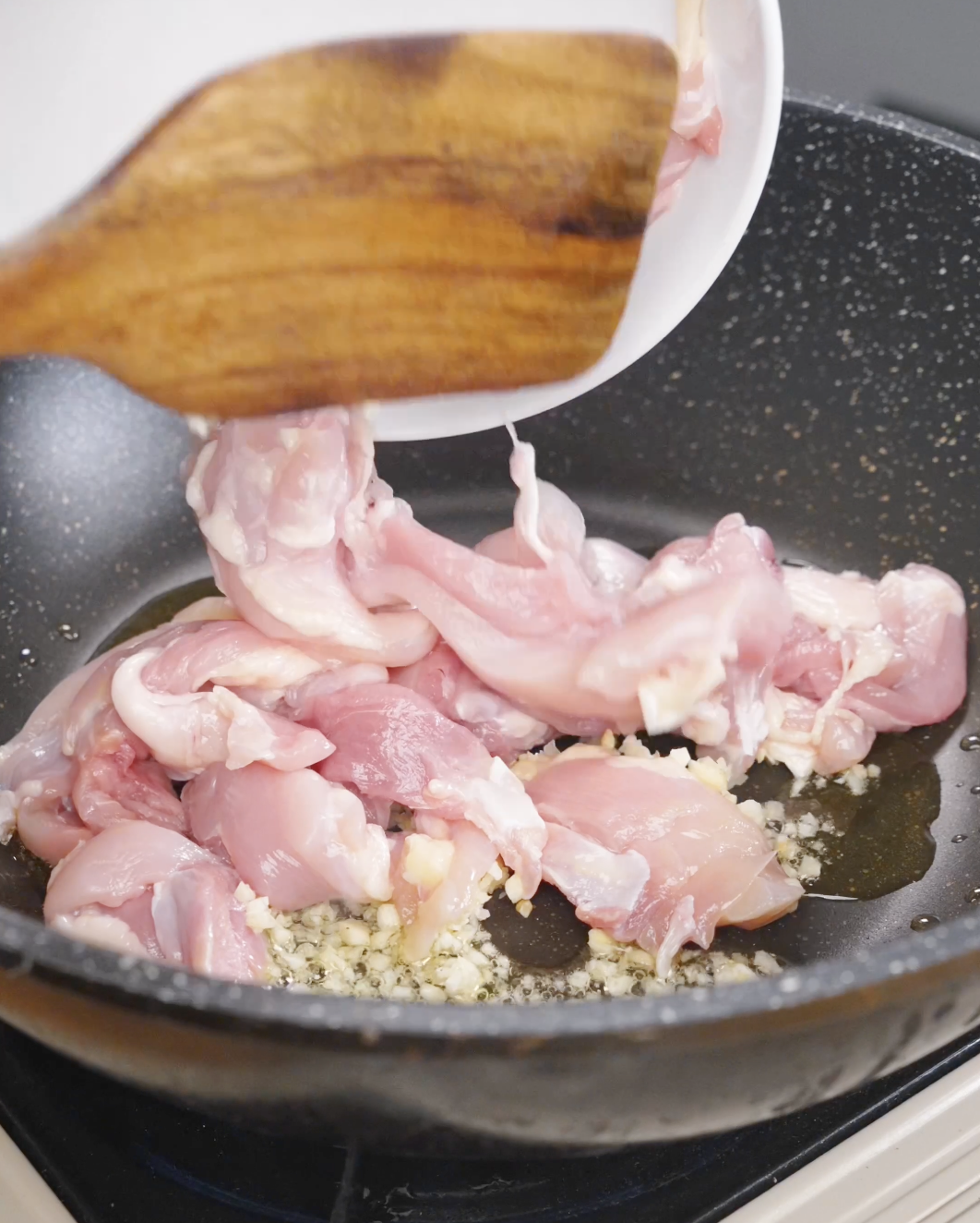 Thinly sliced chicken thighs being added to a hot pan with minced garlic to start this Pad See Ew Recipe.