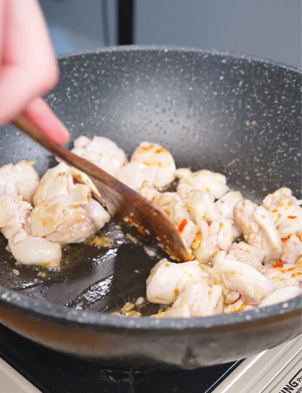 Chicken thighs being stirred in the pan with garlic and Thai chilies while making this Three Cup Chicken Recipe.