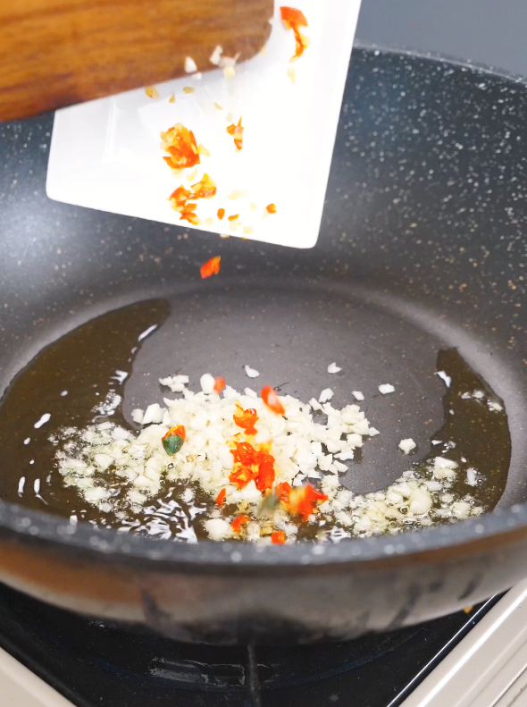 Minced garlic and sliced Thai chilies being added to hot oil to build the flavor base for this Three Cup Chicken Recipe.