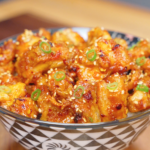 Crispy Chili Oil Chicken Recipe served in a bowl over rice and garnished with sesame seeds and sliced scallions.