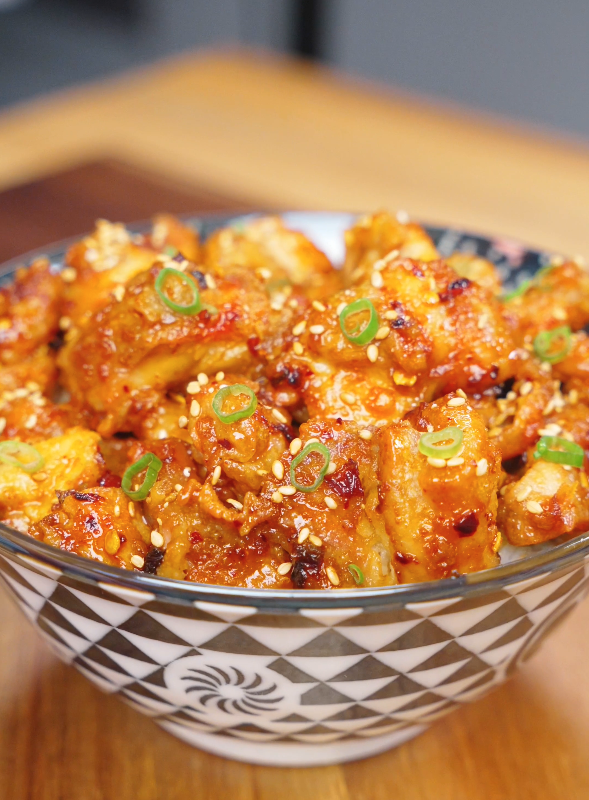 Crispy Chili Oil Chicken Recipe served in a bowl over rice and garnished with sesame seeds and sliced scallions.