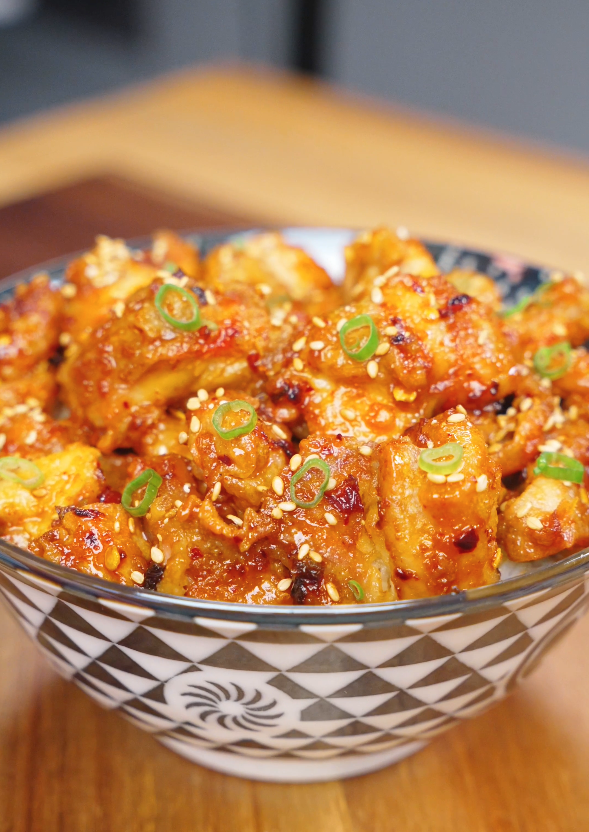 Crispy Chili Oil Chicken Recipe served in a bowl over rice and garnished with sesame seeds and sliced scallions.