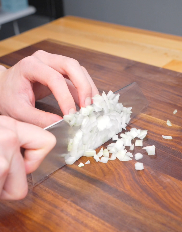 Finely dicing a white onion on a wooden cutting board to prepare the aromatic base for this Gochujang Vodka Pasta Recipe.