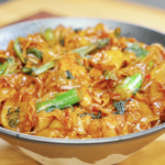 Bowl of Drunken Noodles Recipe made with wide rice noodles, chicken thighs, Chinese broccoli, and Thai basil. The noodles are coated in a rich sauce and garnished with fresh vegetables.