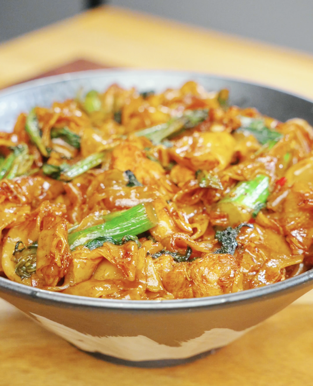 Bowl of Drunken Noodles Recipe made with wide rice noodles, chicken thighs, Chinese broccoli, and Thai basil. The noodles are coated in a rich sauce and garnished with fresh vegetables.