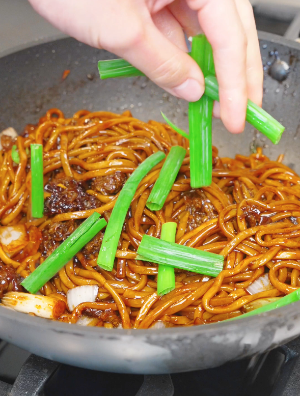 Fresh scallion greens being added to Mongolian Beef Noodles Recipe before the final toss.