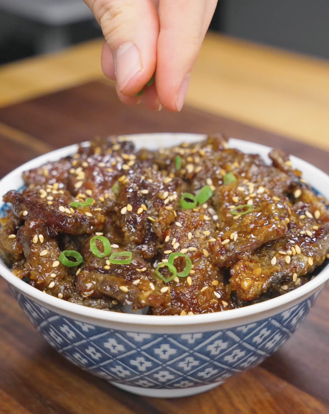 Fresh scallions being sprinkled over a bowl of Crispy Honey Garlic Beef Recipe. The garnish adds freshness, color, and contrast to the sweet and savory beef.