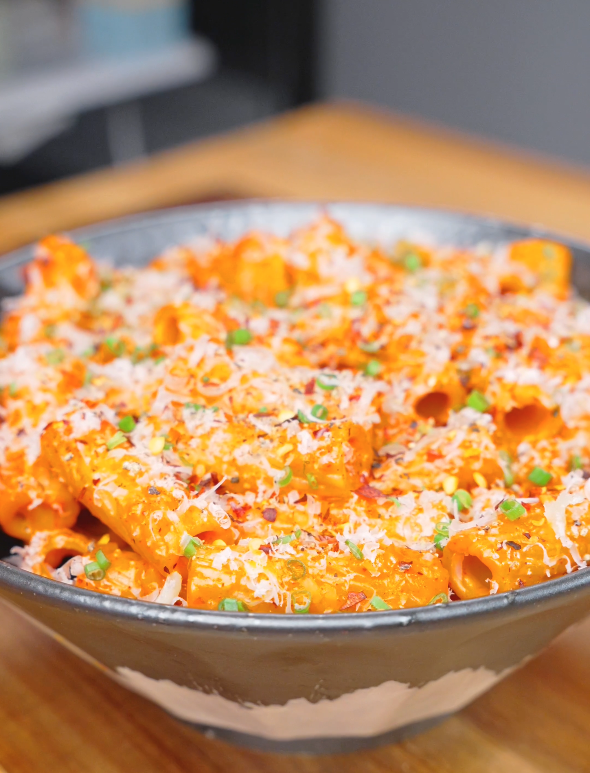 A bowl of creamy Gochujang Vodka Pasta Recipe topped with freshly grated parmesan, chopped chives, black pepper, and red pepper flakes.