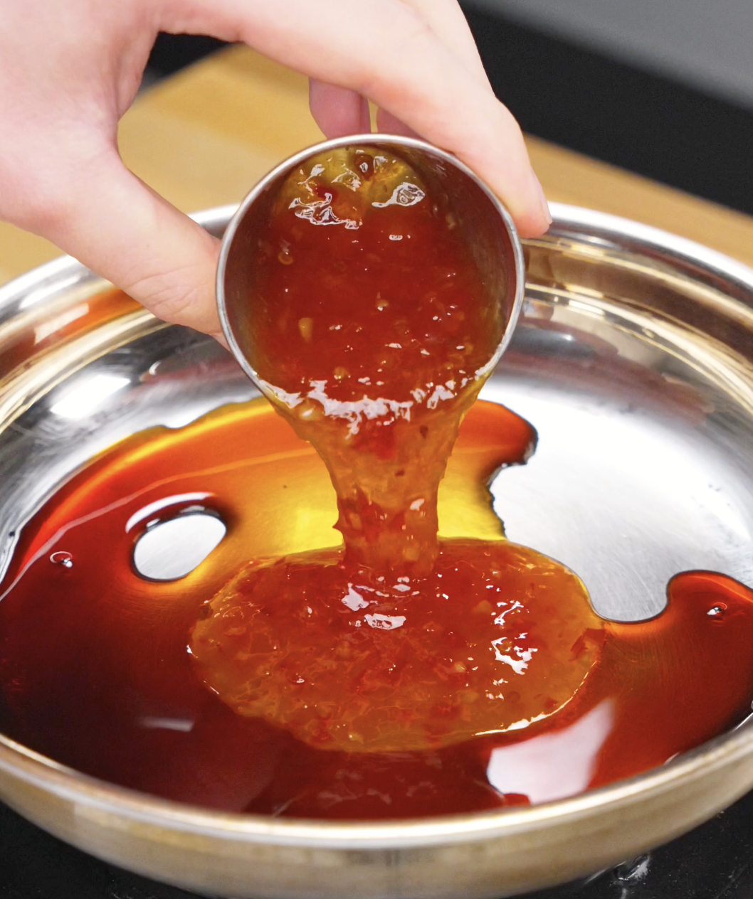 Sweet chili sauce being added to a pan with soy sauce, rice vinegar, water, and garlic to create the glaze for this Crispy Chili Beef Recipe.