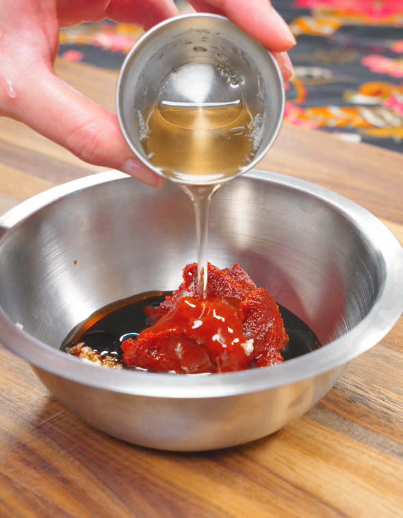 Rice syrup being poured into a bowl with gochujang, soy sauce, sesame oil, garlic, and ginger for the Spicy Cold Noodles Recipe sauce.