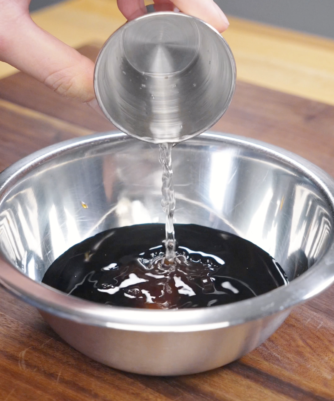 Water being added to a bowl with dark soy sauce, light soy sauce, oyster sauce, rice vinegar, and sugar to create the sauce for this Pad See Ew Recipe.