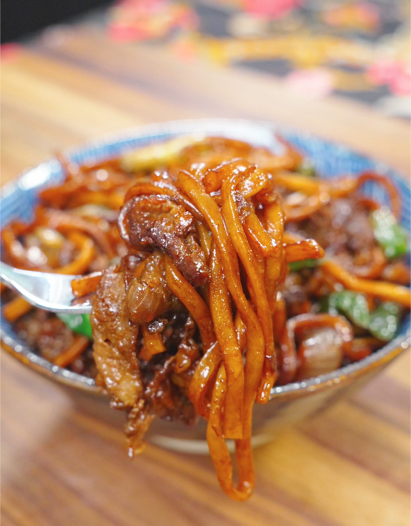 A fork lifting a bite of Mongolian Beef Noodles Recipe with tender beef and sauce-coated noodles.