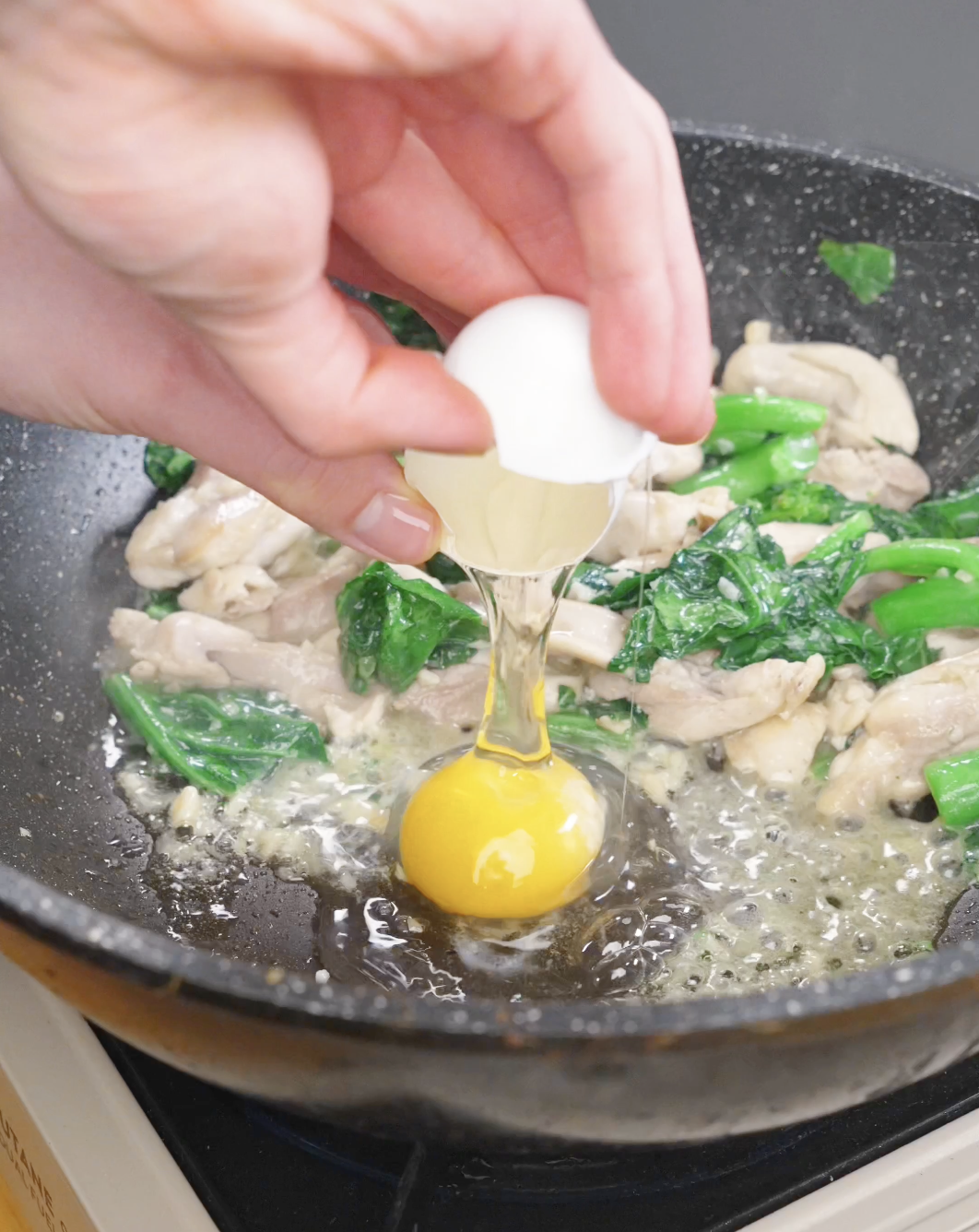 An egg being cracked into the pan and cooked with the chicken and Chinese broccoli for this Pad See Ew Recipe.