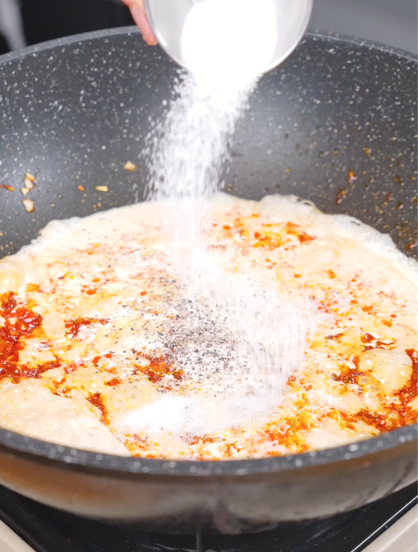 Salt, black pepper, and sugar being added to the creamy gochujang vodka sauce before tossing with the pasta in this Gochujang Vodka Pasta Recipe.