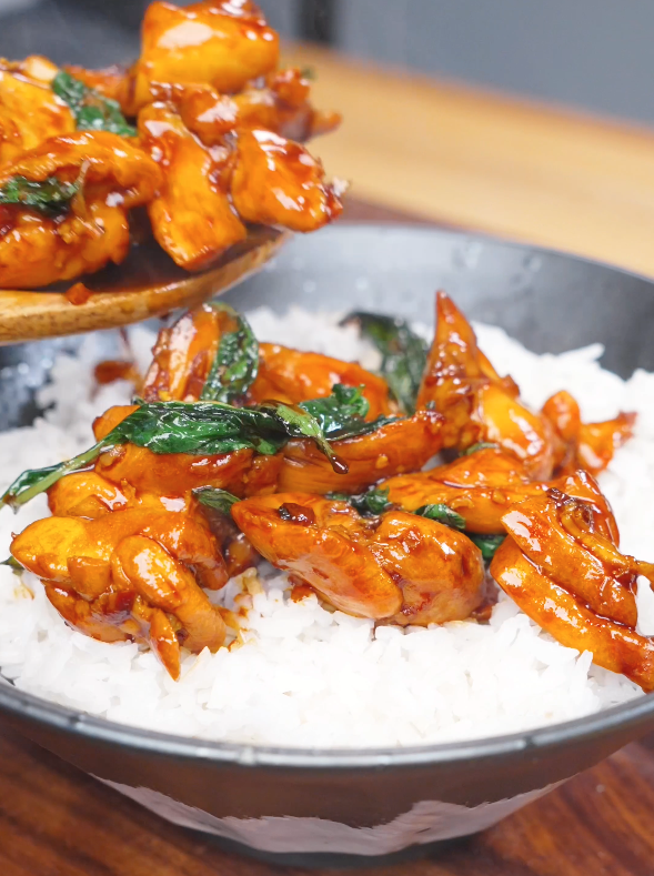 Freshly cooked Three Cup Chicken Recipe being spooned over steamed rice. The chicken is coated in a glossy soy-based sauce and tossed with garlic, Thai chilies, ginger, and Thai basil.