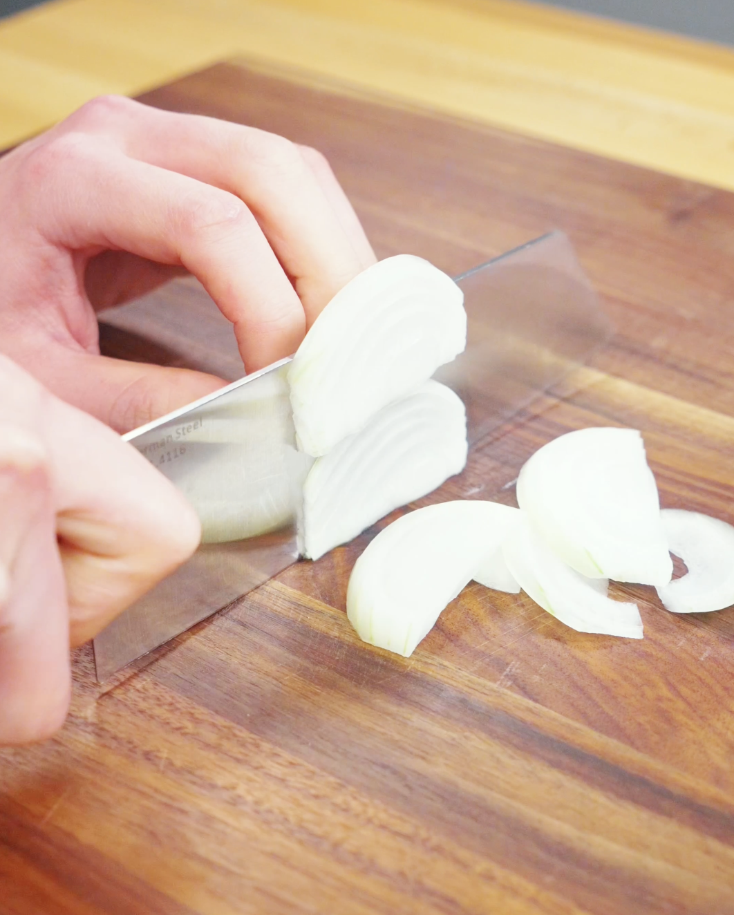 Onion being thinly sliced on a cutting board for a Drunken Noodles Recipe. Thin slices cook quickly and add sweetness to the stir-fried noodles.