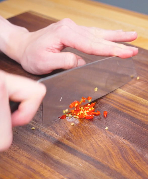 Fresh Thai chilies being finely sliced on a cutting board for this Three Cup Chicken Recipe.