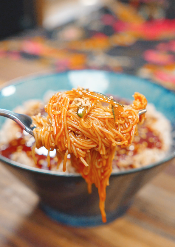 A fork lifting a bite of Spicy Cold Noodles Recipe coated in a savory gochujang sauce with sesame seeds.