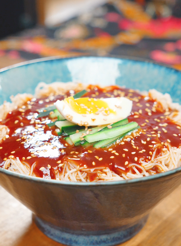 Spicy Cold Noodles Recipe served in a bowl with gochujang sauce, cucumber, boiled egg, and sesame seeds.