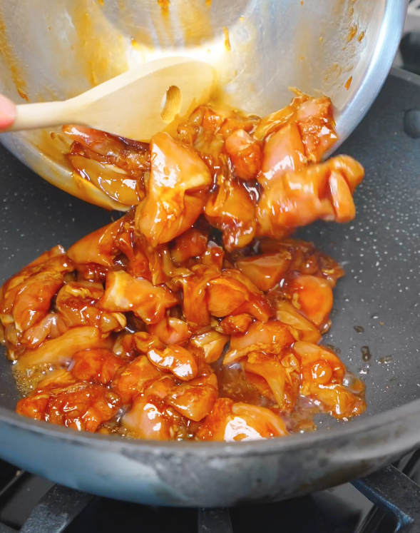 Marinated chicken thighs being poured into a hot pan to cook in the flavorful sauce for this Sweet Honey Chicken Recipe.