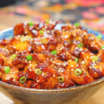 A bowl of Sweet Honey Chicken Recipe coated in a sticky honey glaze and topped with sesame seeds and fresh scallions.