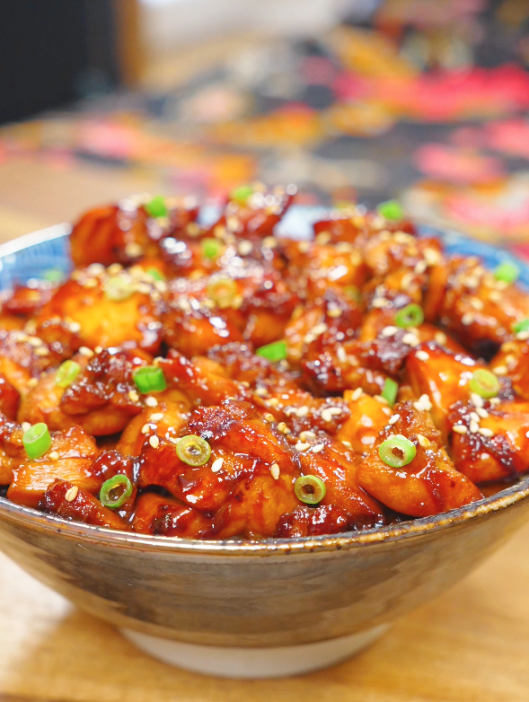 A bowl of Sweet Honey Chicken Recipe coated in a sticky honey glaze and topped with sesame seeds and fresh scallions.