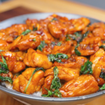 A bowl of Three Cup Chicken Recipe served over steamed rice with tender chicken coated in a glossy soy-based sauce and finished with Thai basil.