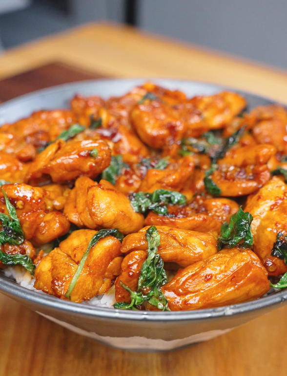 A bowl of Three Cup Chicken Recipe served over steamed rice with tender chicken coated in a glossy soy-based sauce and finished with Thai basil.