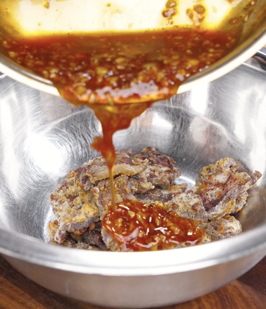 Crispy air fried beef being coated in a glossy sweet chili garlic sauce for this Crispy Chili Beef Recipe.