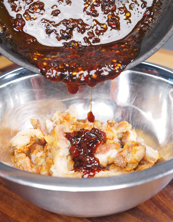Crispy air-fried chicken being coated with a sweet and spicy chili oil sauce in a mixing bowl.