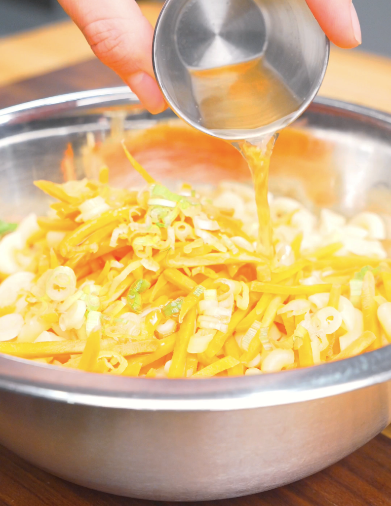 Apple cider vinegar being poured over macaroni, shredded carrots, and scallions for Hawaiian Mac Salad Recipe.