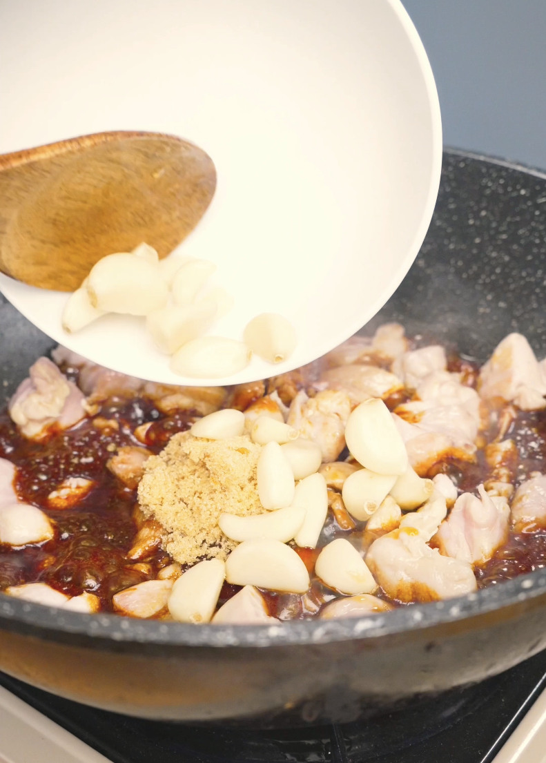 Brown sugar and garlic cloves being added to the chicken and sauce in the pan for Sticky Garlic Chicken Recipe.