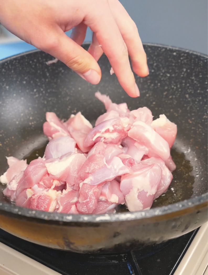 Bite-sized raw chicken pieces being added to the pan for Sticky Garlic Chicken Recipe.