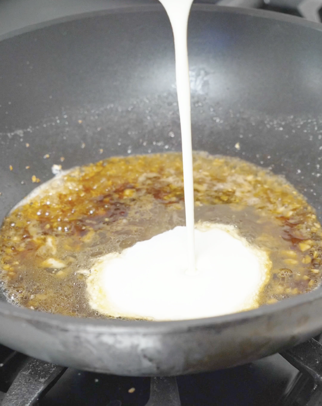 Heavy cream being poured into a garlic butter sauce for the Creamy Garlic Butter Noodles Recipe.