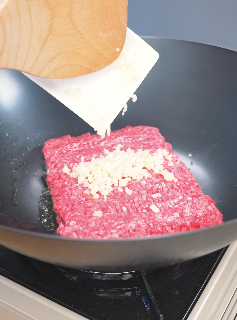 Minced garlic being added onto raw ground beef in a wok for Garlic Ground Beef Recipe.